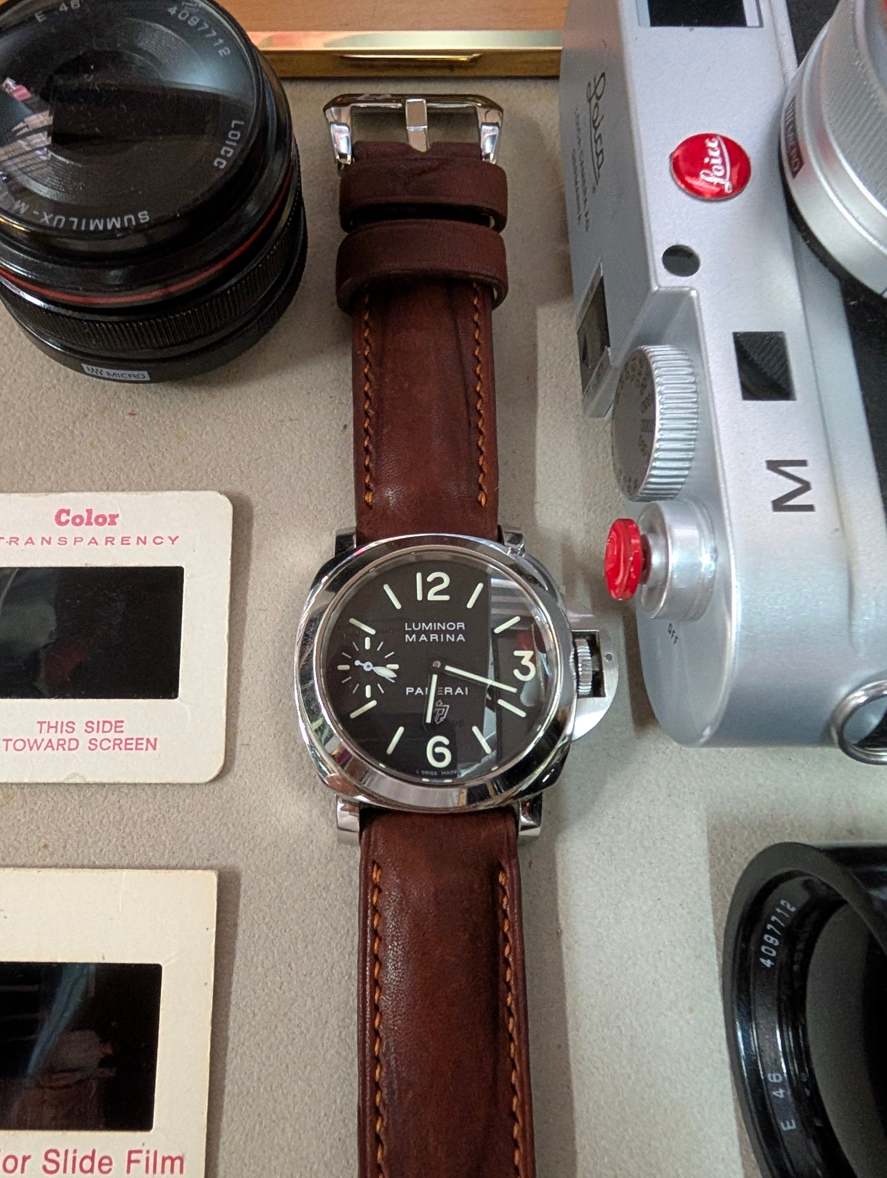 Watch with brown leather strap on a surface with camera equipment and film reels.